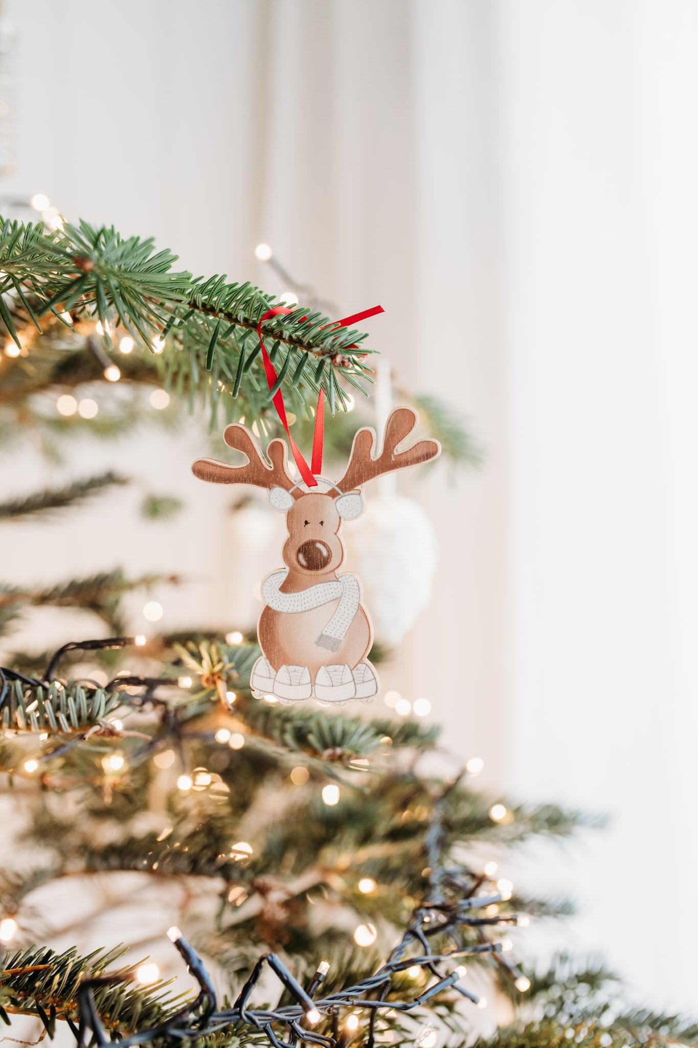 reindeer wearing ear muffs scarf and ice skates wooden decoration on a christmas tree with twinkly lights