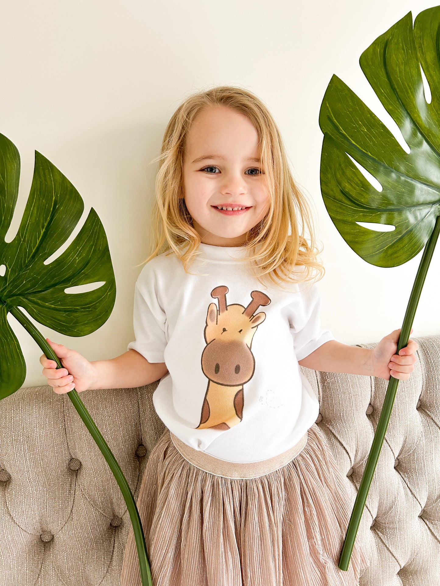 girl wearing a white cotton t-shirt with a safari wild giraffe printed design holding two jungle green leaves