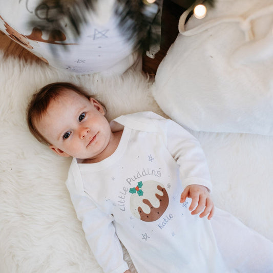 baby wearing little pudding sleepsuit lying under a christmas tree