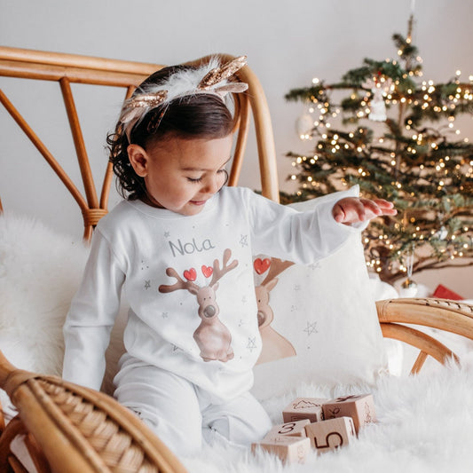 toddler girl wearing reindeer christmas pyjamas playing with wooden blocks by a christmas tree