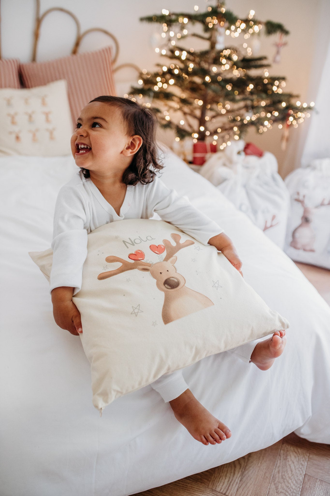 girl sat on a ed holding a personalised christmas cushion with a magical reindeer design