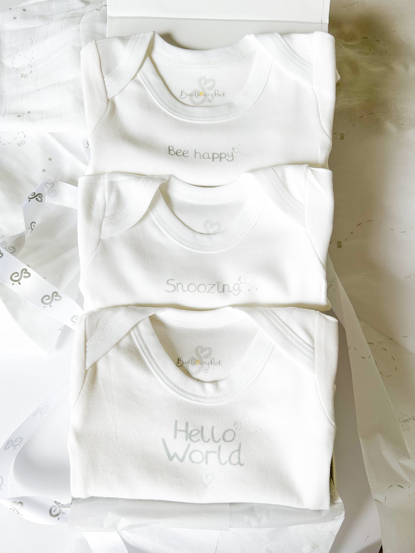 three white baby bodysuit vests with neutral silver text design in a white gift box with satin ribbon wrap