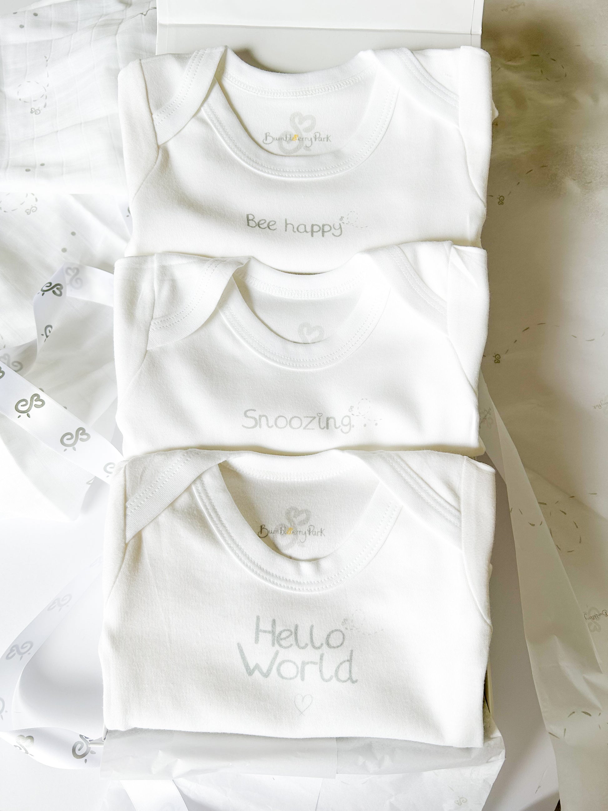 three white baby bodysuit vests with neutral silver text design in a white gift box with satin ribbon wrap