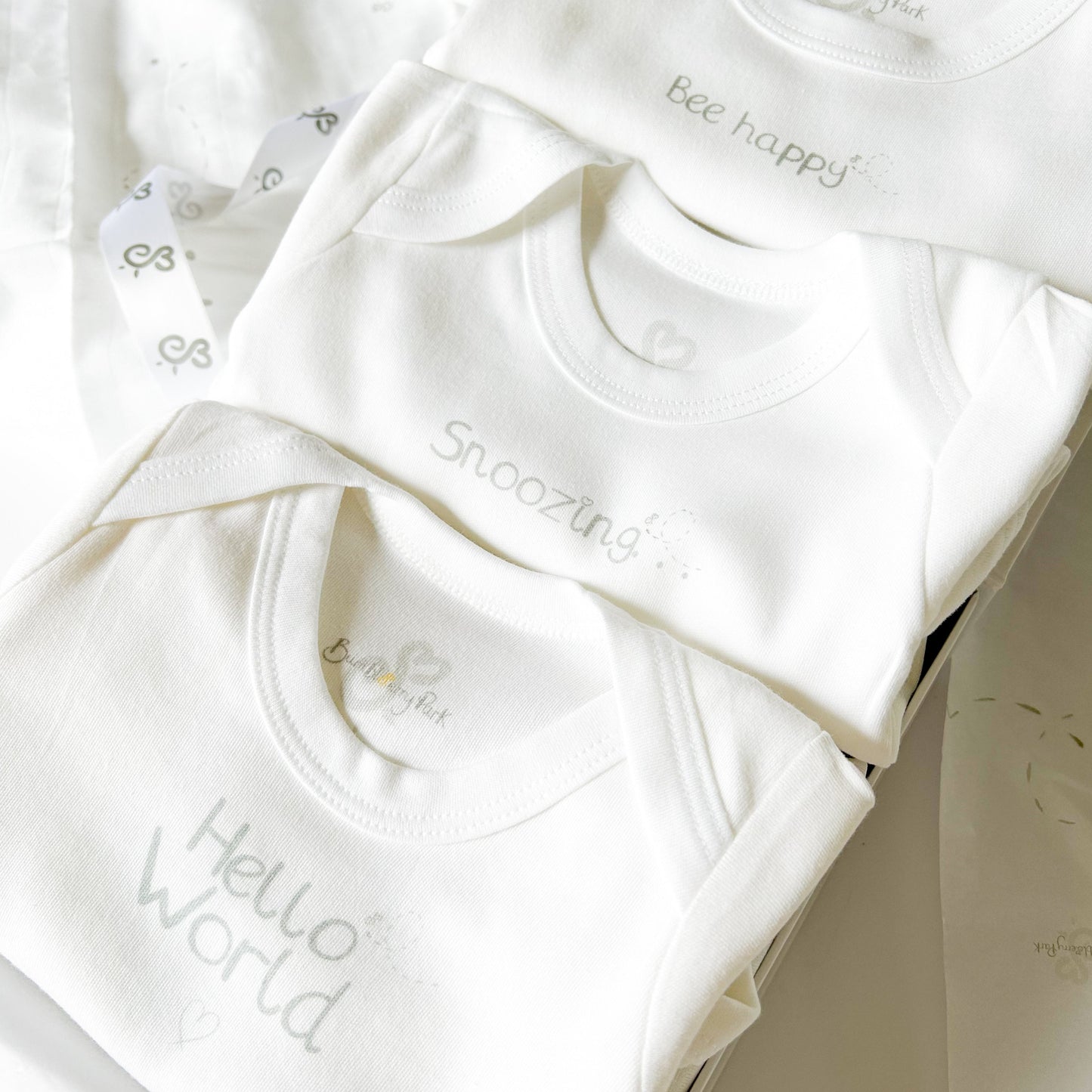 set of 3 baby bodysuits with neutral grey typography designs "bee happy" "snoozing" and "hello world" in a luxury gift box