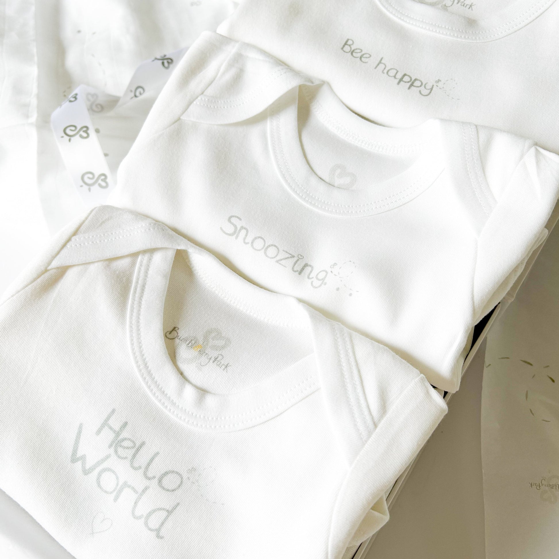 set of 3 baby bodysuits with neutral grey typography designs "bee happy" "snoozing" and "hello world" in a luxury gift box