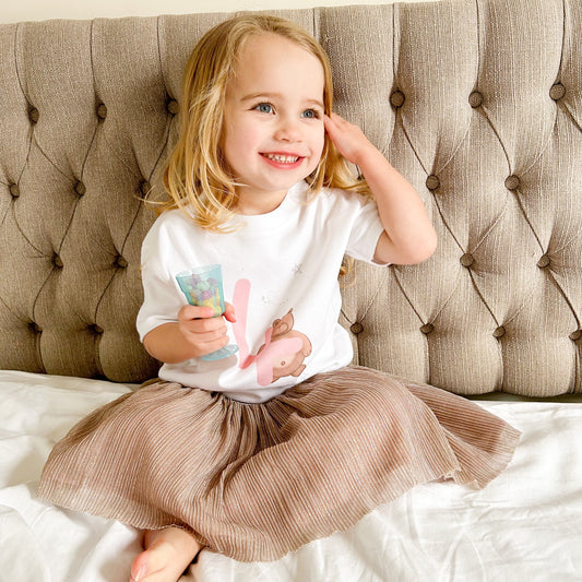 toddler girl smiling wearing a personalised birthday top with a woodland brown bear illustration print and pink age 4