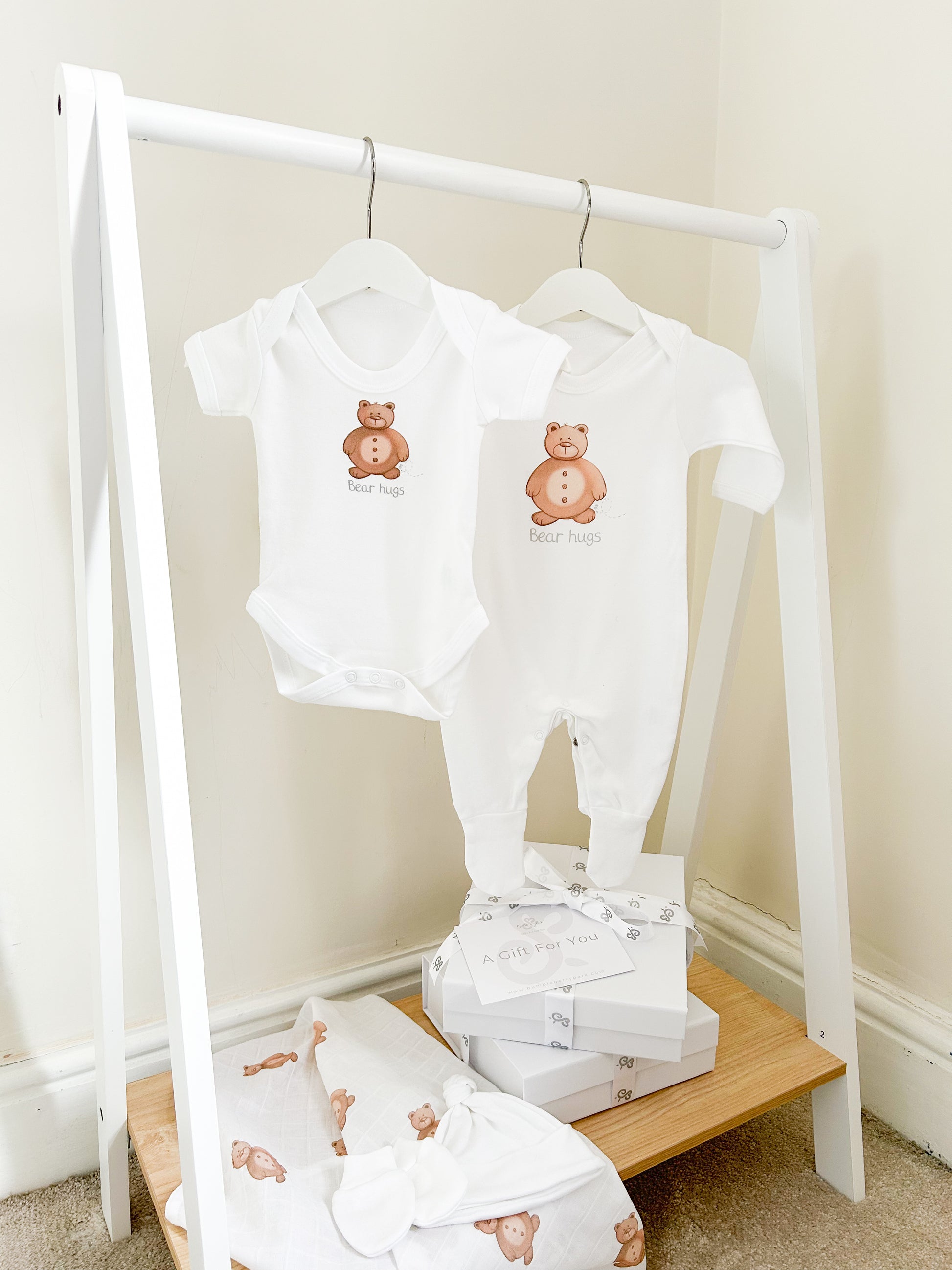 child's clothes rail with a white bodysuit and sleepsuit set with cute teddy bear print with hat and mitten and bear printed muslin cloth with a white gift box