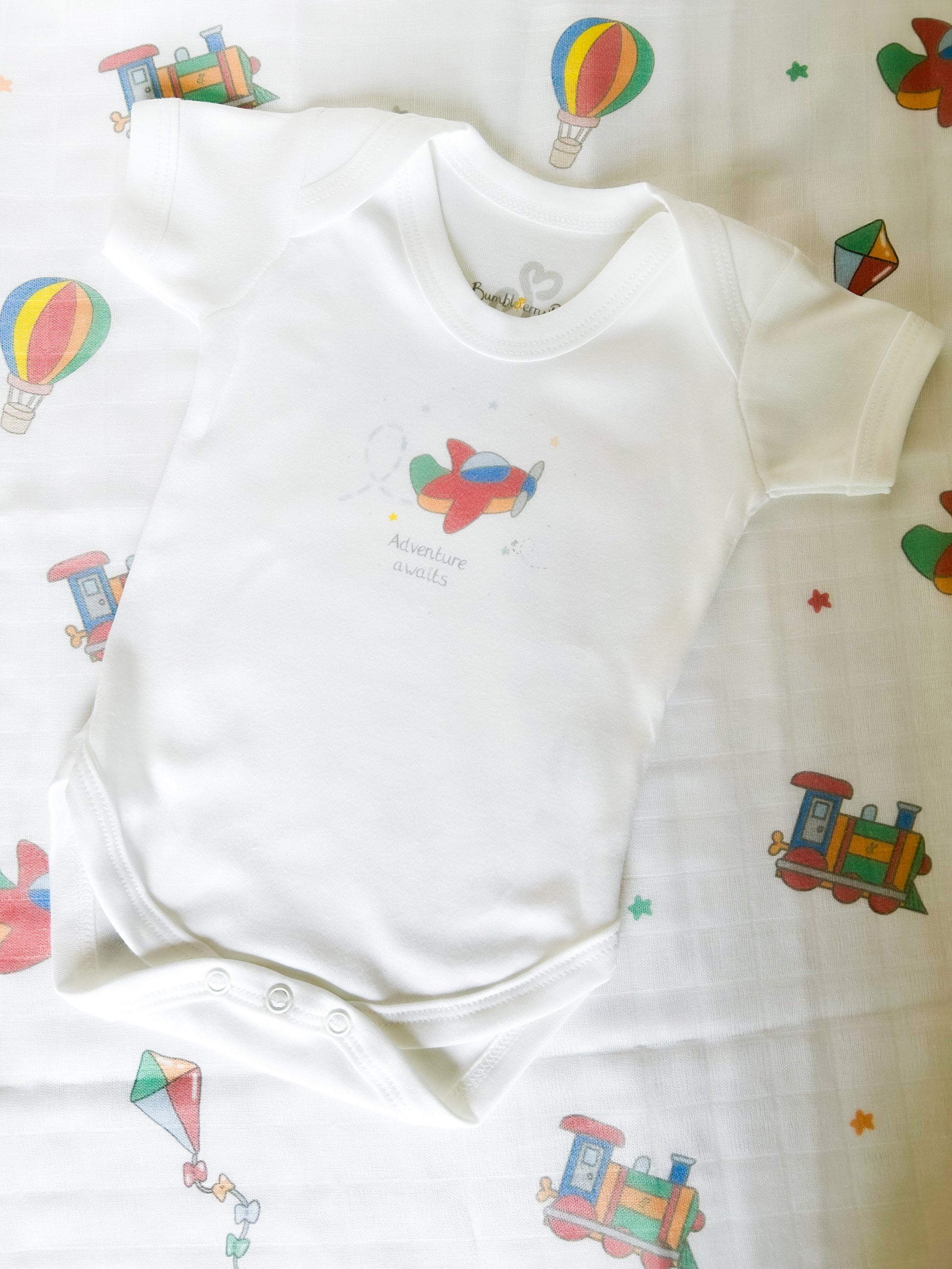 gift set of baby bodysuit and muslin cloth with travel and transport theme print in bright primary colours