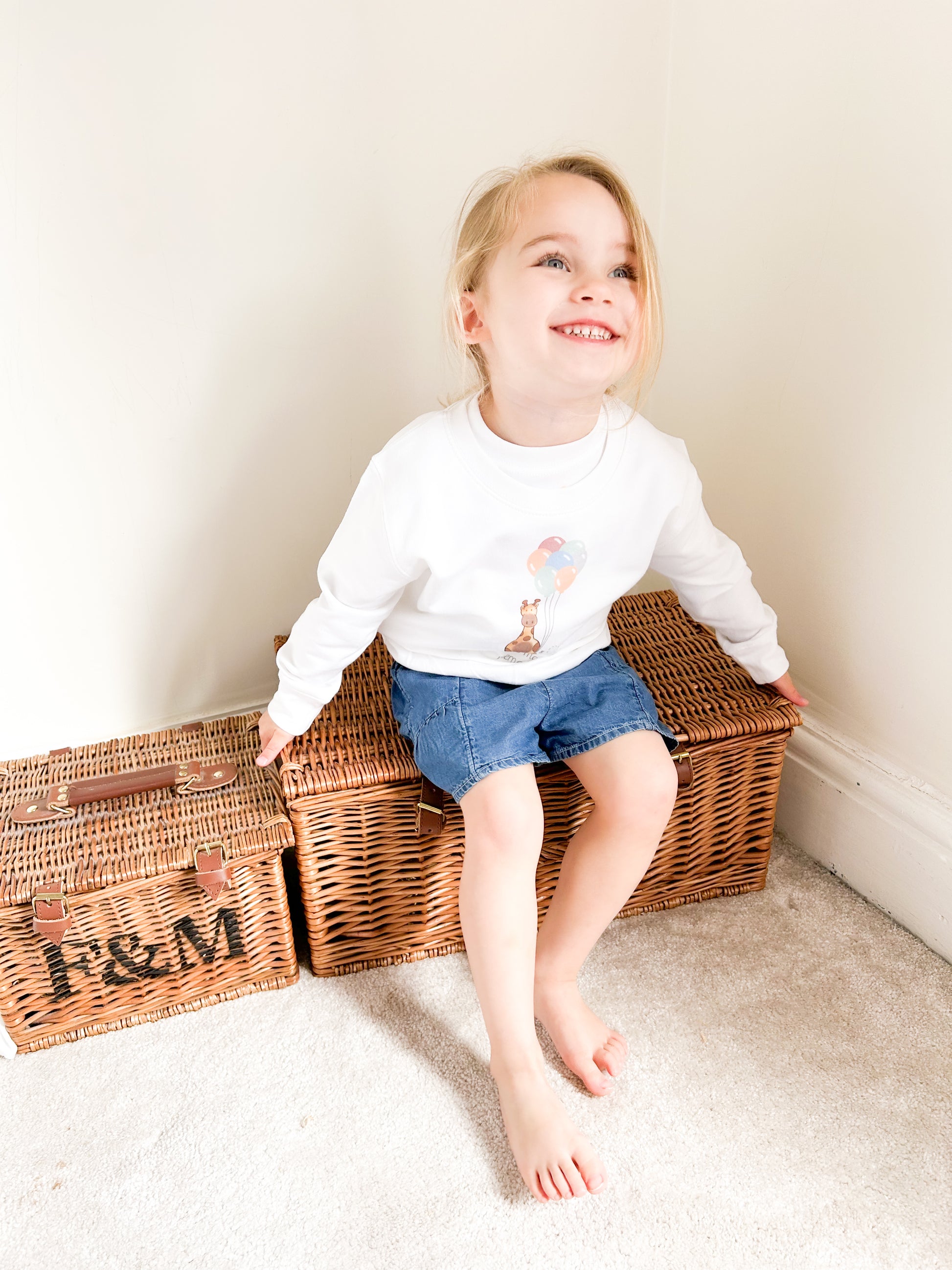girl sat on a picnic hamper wearing summer outfit of white giraffe design sweatshirt and shorts