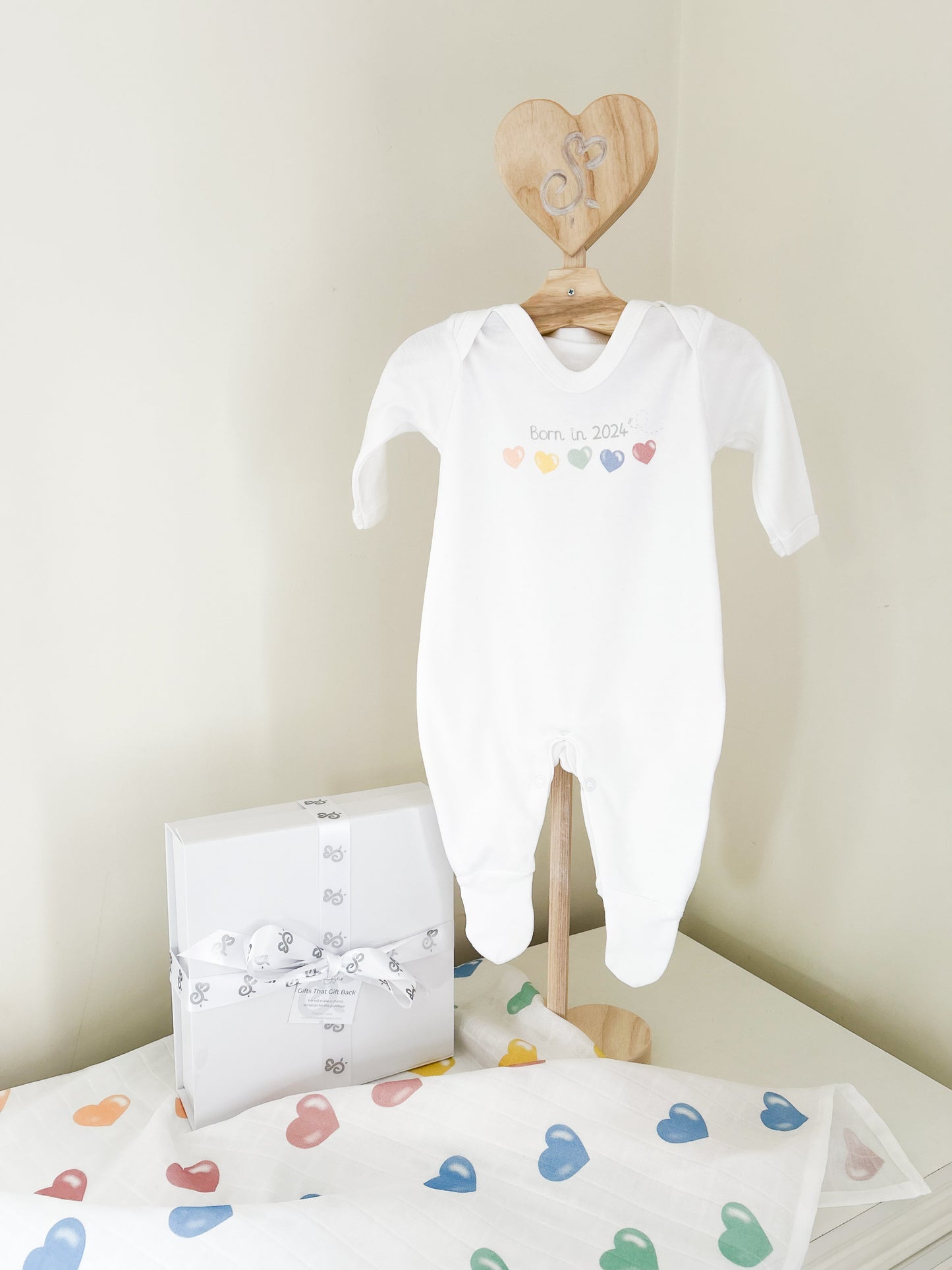newborn white baby bodysuit with Born in 2024 printed on the front with colourful love hearts in peach, yellow, green, blue and red for newborn baby gift