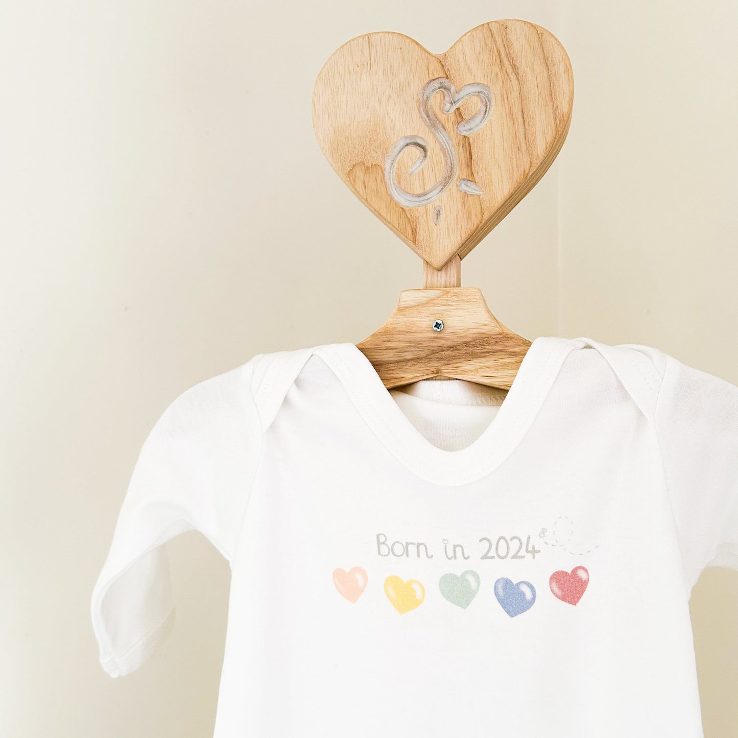 close up on white baby sleepsuit with "born in 2024" quote and bright rainbow colour love heart printed design