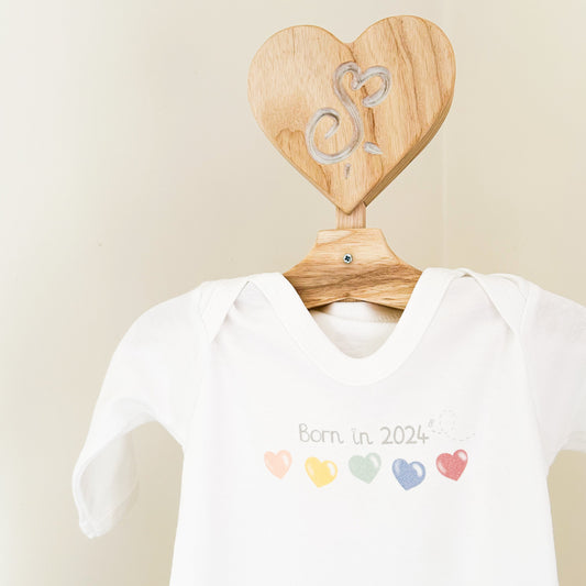 close up on white baby sleepsuit with "born in 2024" quote and bright rainbow colour love heart printed design