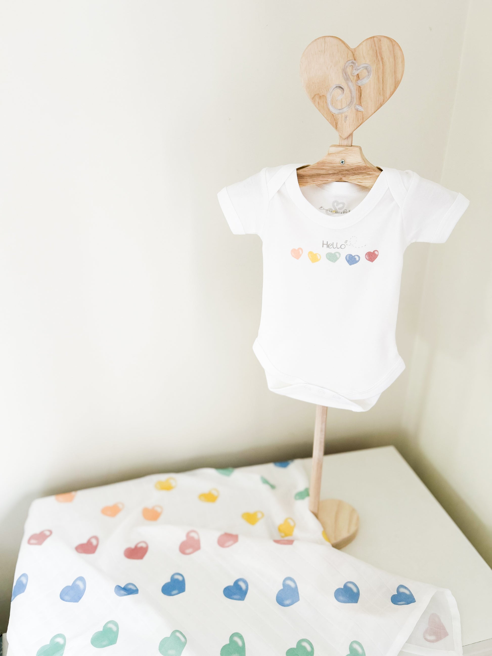 clothes stand with white baby vest on it printed with a colourful set of hearts and "hello" message with a matching baby love heart muslin square
