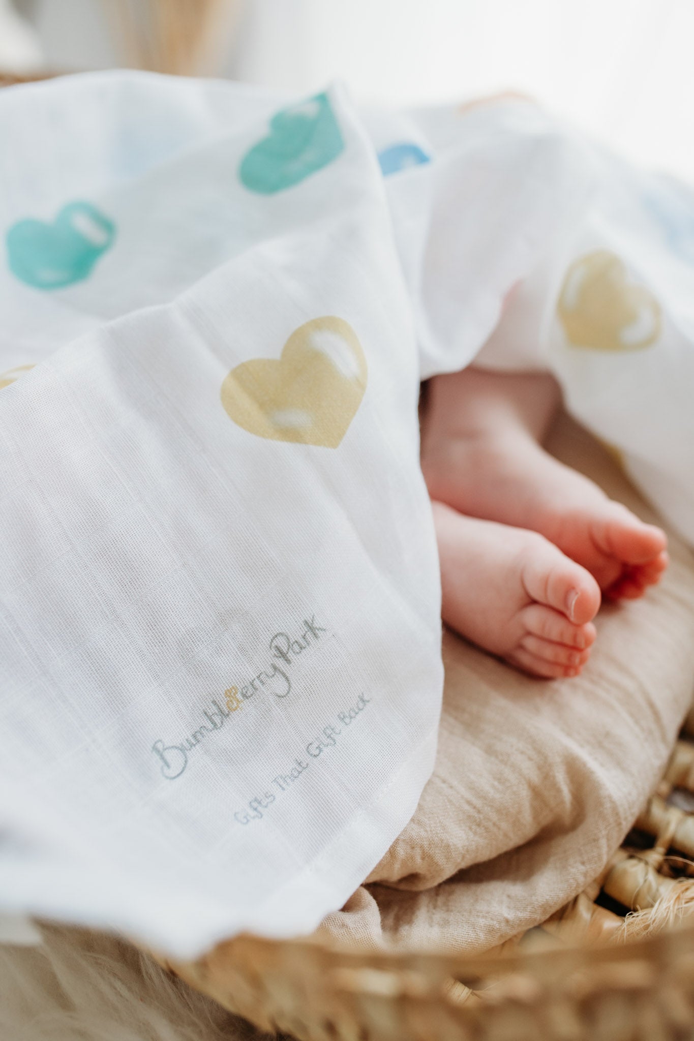 baby toes underneath a colourful heart printed muslin cloth