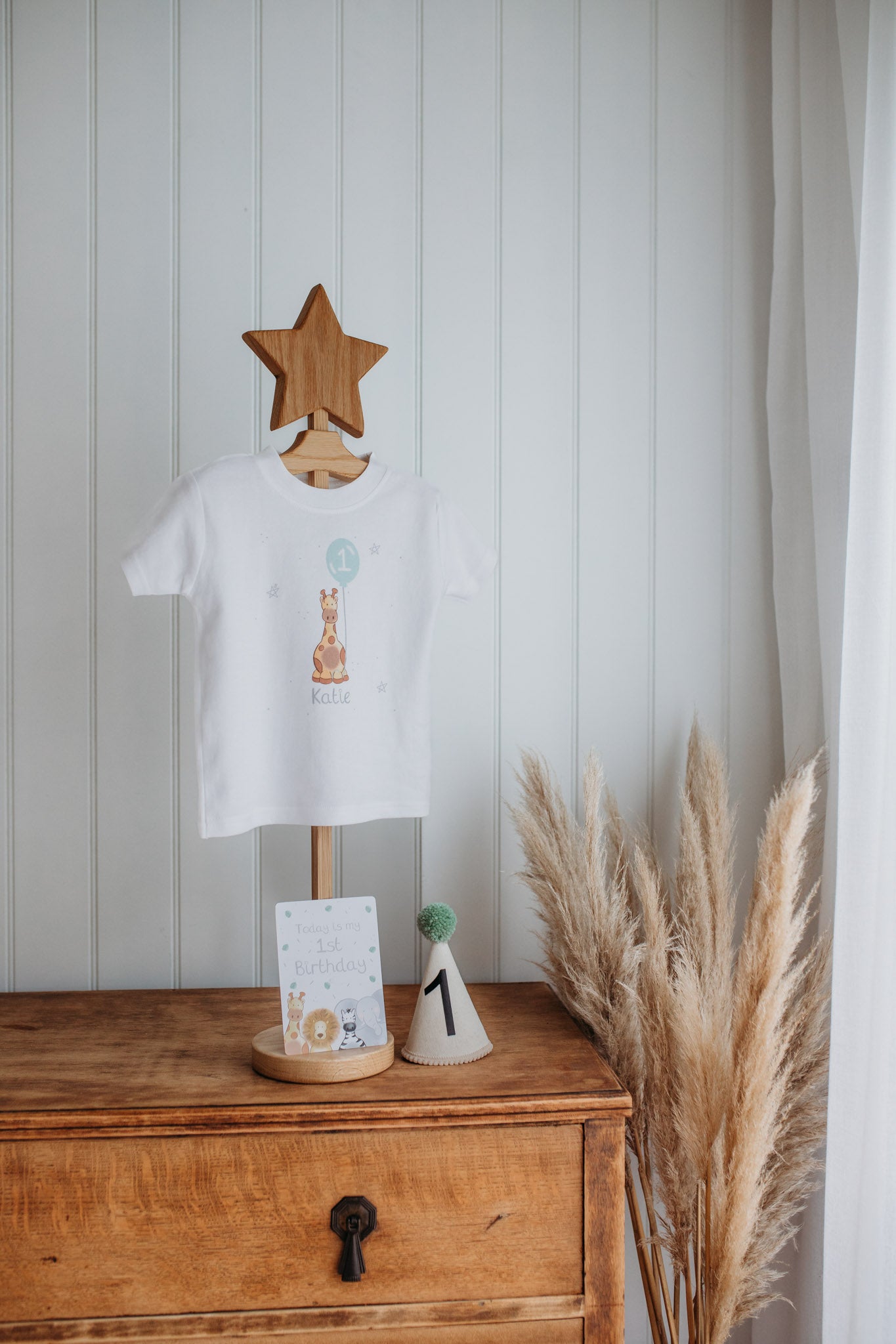 clothes hanger holding a personalised 1st birthday t-shirt with a safari giraffe character print and girls name with a 1st birthday party hat